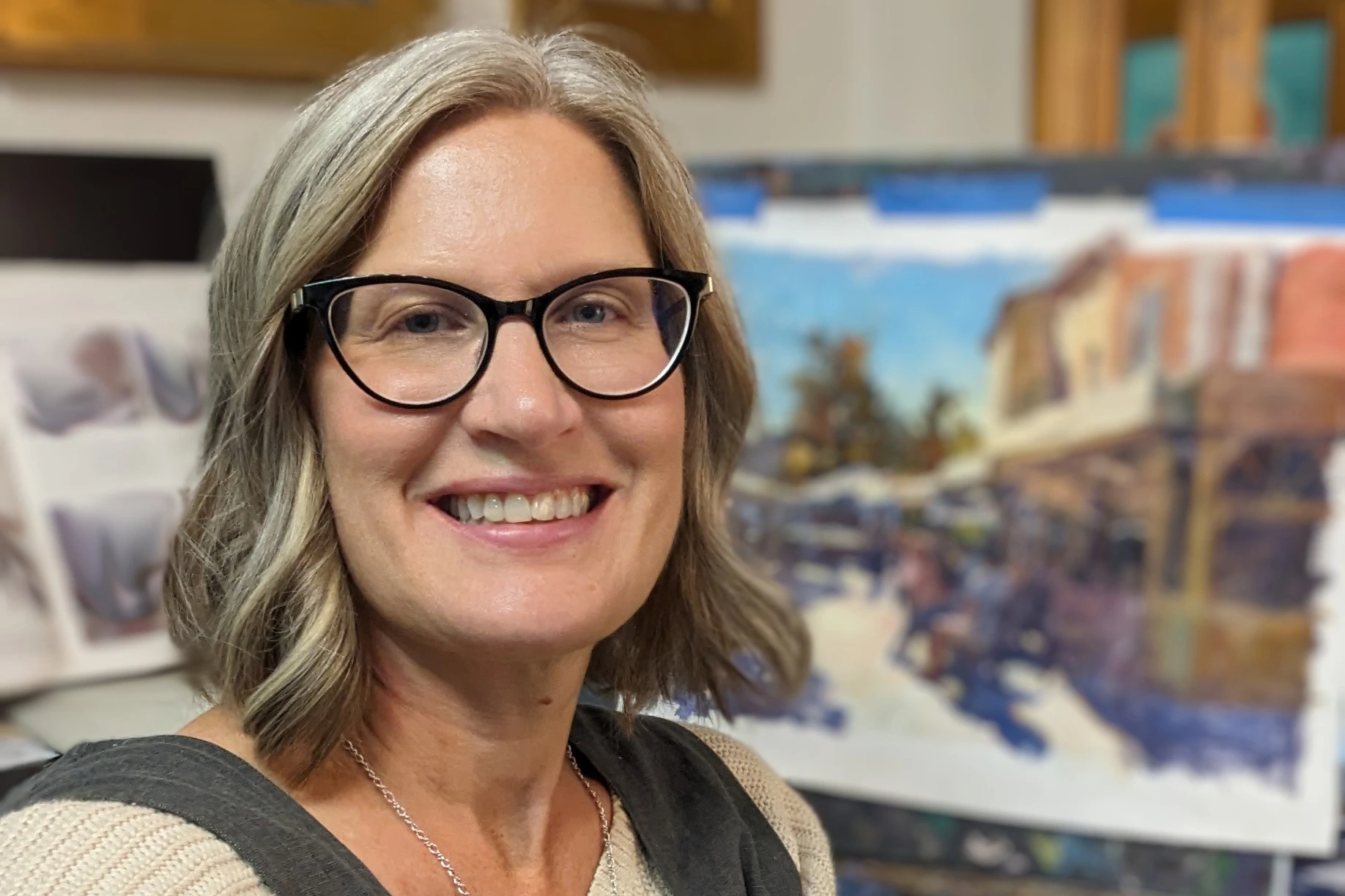 smiling woman with glasses in art studio beside painting