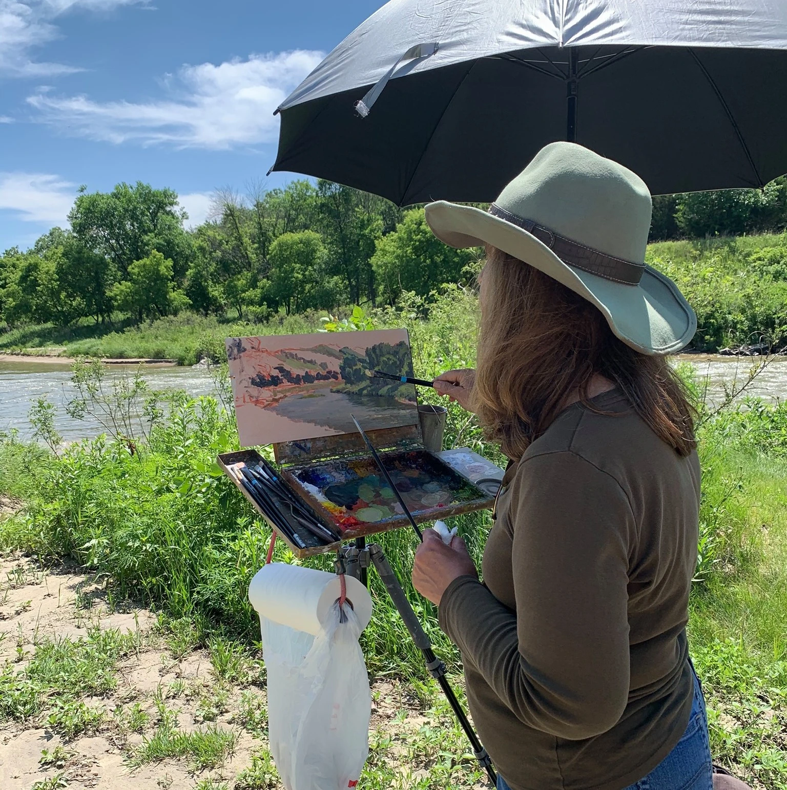 Artist painting riverside landscape at an outdoor easel
